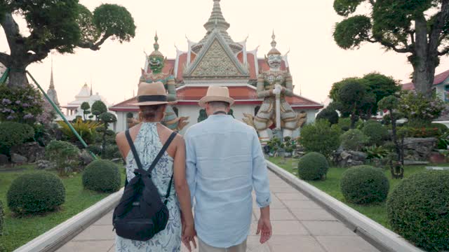 不同种族的夫妇快乐的游客在他们的假期旅行，并持有旅游地图和指向Wat Arun Temple在曼谷，泰国视频下载