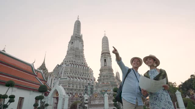 不同种族的夫妇快乐的游客在他们的假期旅行，并持有旅游地图和指向Wat Arun Temple在曼谷，泰国视频素材