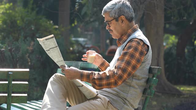 老人在公园长椅上喝茶看报纸视频素材