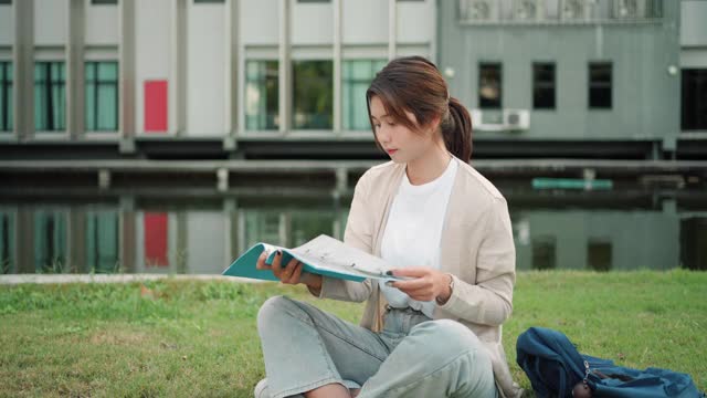 亚洲女子大学的学生坐在校园草地上看快乐和在公园看书。视频素材