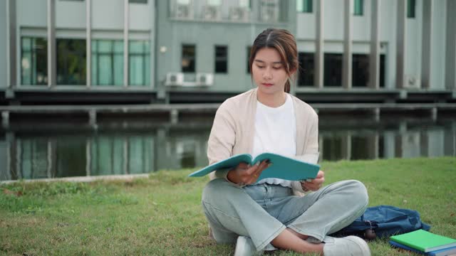 亚洲女子大学的学生坐在校园草地上看快乐和在公园看书。视频素材