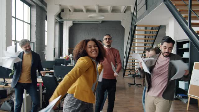 快乐的商务人士在办公室跳舞，扔文件玩乐的慢镜头视频素材