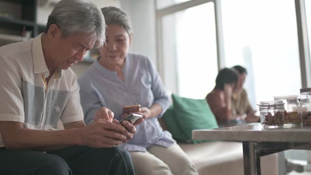 亚洲华人老年夫妇老花眼在周末闲暇时间试图在客厅学习使用智能手机有困难视频下载