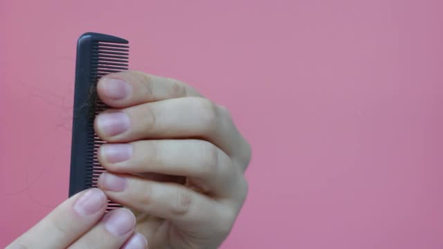 女人的手拿着梳子，头发落在粉红色的背景上。视频素材