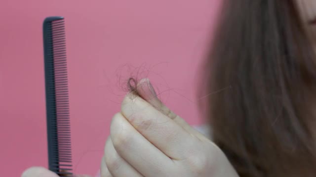 女孩抱着一缕头发正面看待粉红色的背景，有脱发的观念视频素材