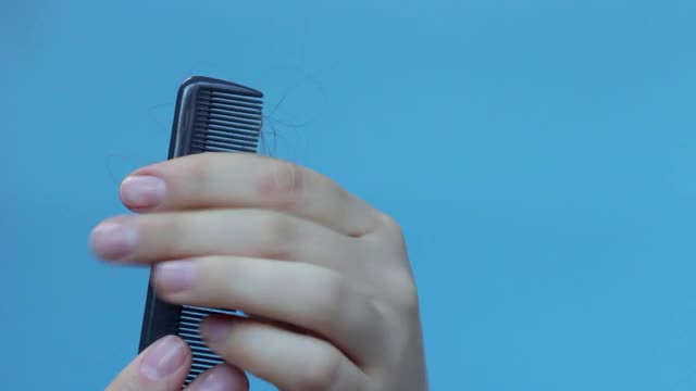 女人的手拿着梳子，头发落在蓝色的背景上。视频素材