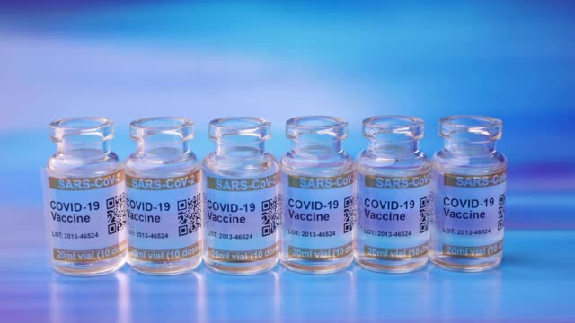 小批COVID-19疫苗瓶，蓝色抽象背景。标签SARS-CoV-2对抗冠状病毒，手放在保护手套放置注射器视频素材