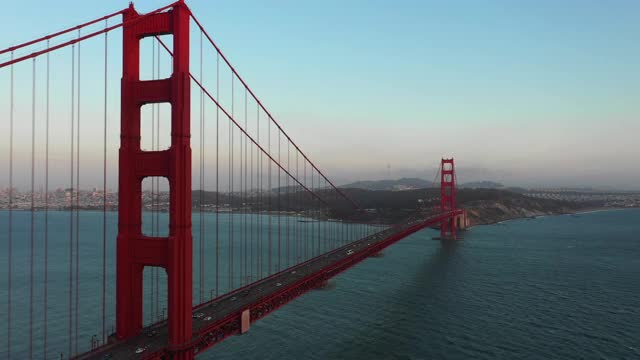 航拍拍摄金门大桥上的车辆在海湾上，无人机在日落时分的天空中向前飞过著名的地标——旧金山，加利福尼亚视频下载