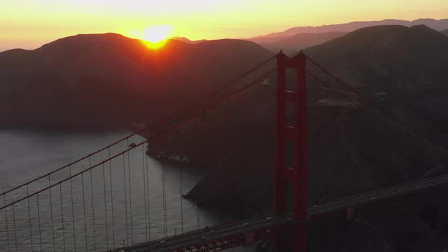 航拍金门大桥上的汽车，在日落时分，无人机朝着海湾上空的著名地标飞去——旧金山，加利福尼亚视频素材