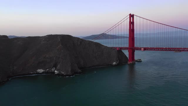 航拍的金门大桥在海湾附近的城市日落，无人机飞向著名的桥梁上的车辆对着天空的山-旧金山，加利福尼亚视频素材