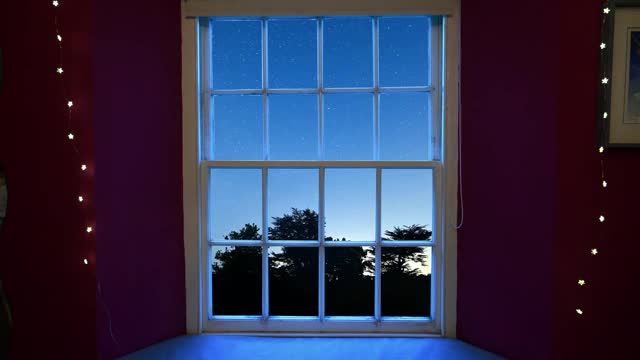 透过一扇窗户的时间推移，在晴朗的夜空中显示星星的轮廓，在前景中树木的剪影视频素材