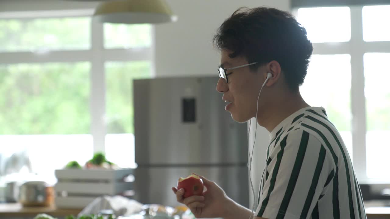 一名亚裔中国男子在家里一边吃着苹果早餐，一边通过网络视频会议向他的网友们挥手致意视频下载