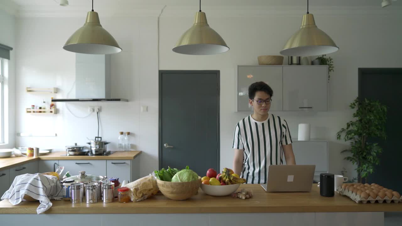 一名亚裔中国男子在家里一边吃着苹果早餐，一边通过网络视频会议向他的网友们挥手致意视频下载