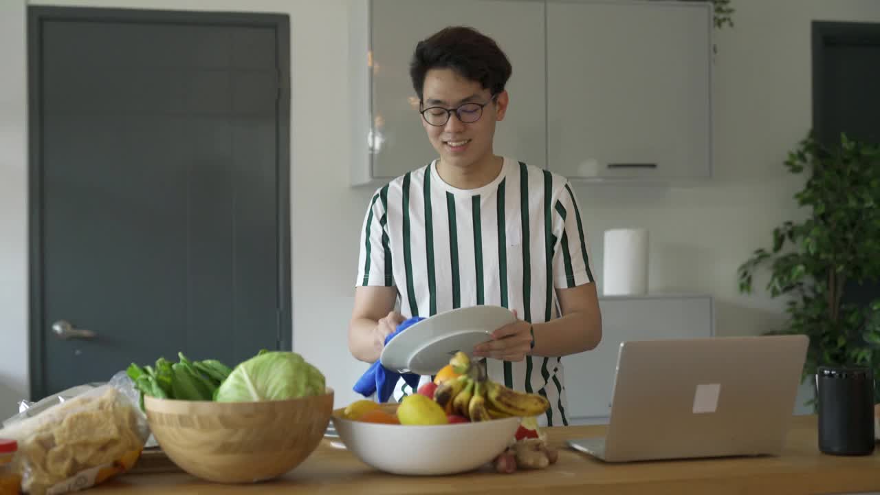 一名亚裔中国男子在家里洗碗的时候通过视频会议和网友聊天视频下载