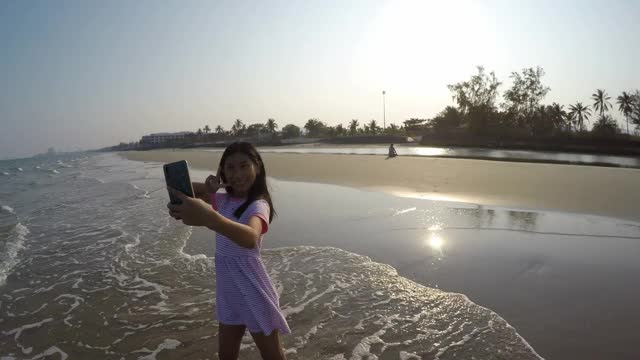 快乐的亚洲女孩自拍自己和视频电话给家人在海滩在阳光明媚的日子，生活理念。视频下载
