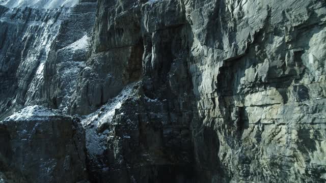 无人机在加拿大落基山脉靠近积雪的岩石悬崖飞行视频下载