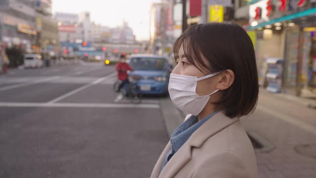在城市中，一名妇女戴着保护面罩穿过街道视频素材