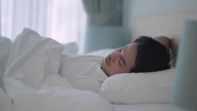 亚洲男人睡甜蜜的梦在一个舒适的午睡在床上在房子里的卧室视频下载