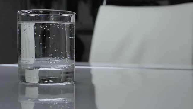 白色的餐桌上放着一杯矿泉水，用玻璃酒杯喝水。视频素材