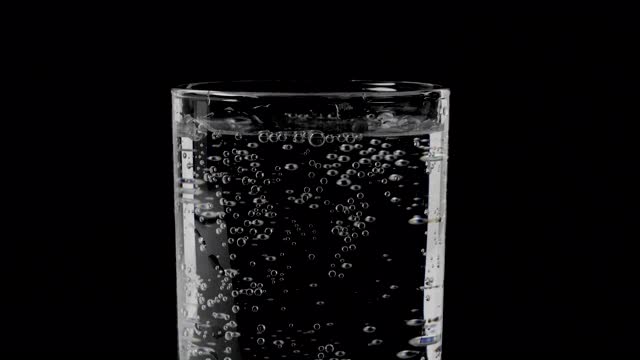 玻璃与矿泉水在一个黑色的背景，水的泡沫在一个杯子的特写，饮用与泡沫的水。视频素材