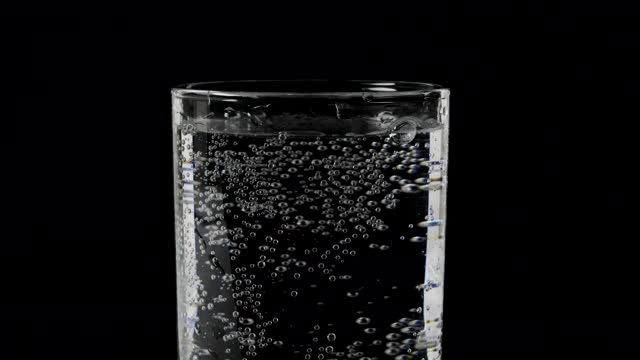 特写水在一个黑色的背景，矿泉水在一个杯子，苏打水，泡沫在一个杯子。视频素材