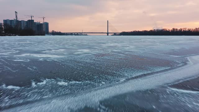 无人机从冰冻的河流上方飞向城市大桥，近距离视频下载