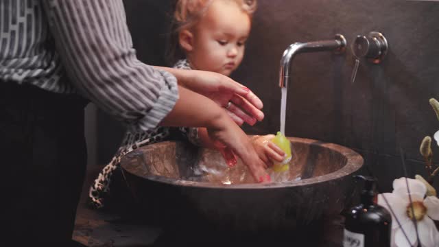 在家里，当女儿在浴室水槽里洗玩具时，女人在用肥皂擦手视频素材