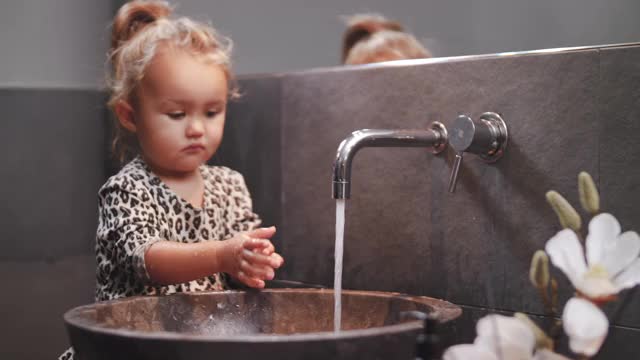 手持拍摄的金发女孩玩，而洗手在浴室水槽在家里视频素材