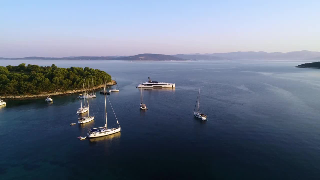 从空中俯瞰大型白色豪华游艇停泊在欧洲地中海国家的一个海湾。美丽的绿岛在夏季。游艇周的航海经验。视频下载