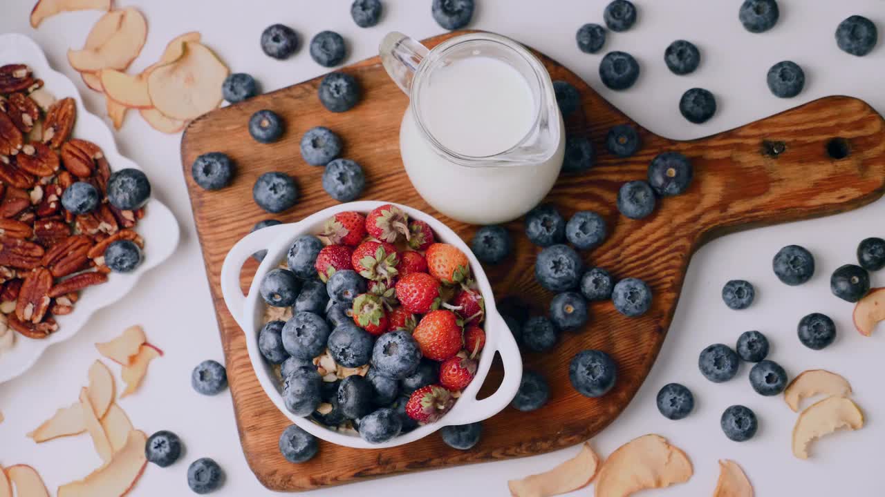 女人把浆果和格兰诺拉麦片，蓝莓和草莓放在陶瓷碗里视频下载