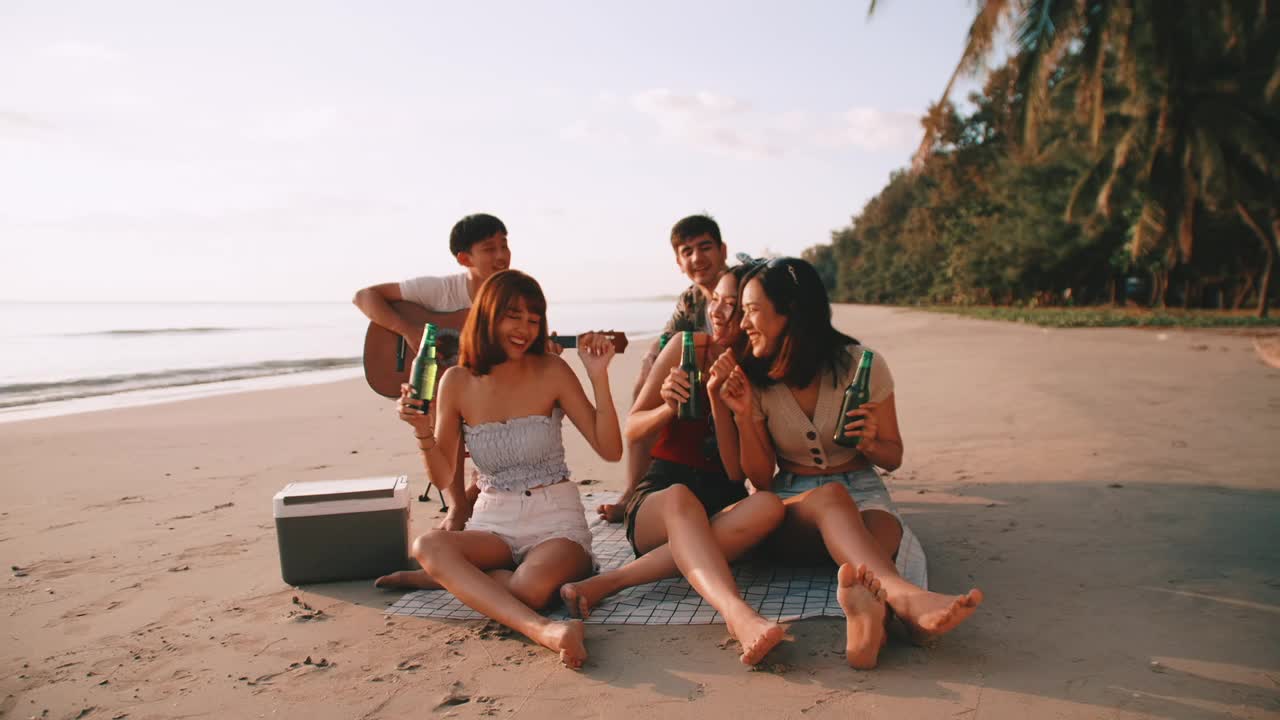 一群年轻的亚洲人在海滩上享受派对。一群朋友在暑假期间喝啤酒。视频素材