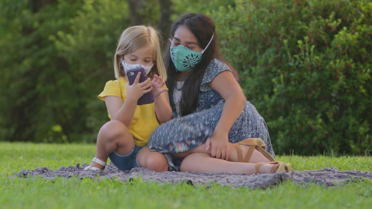 两个小女孩在外面戴着防护口罩一起看智能手机视频素材