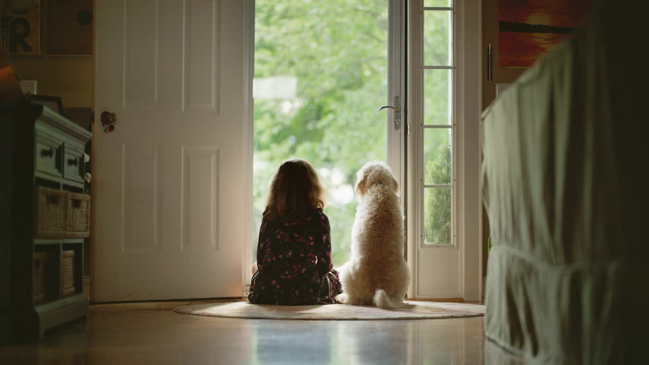 一个年轻的女孩用她的手臂环抱着她的狗，看着前门视频下载