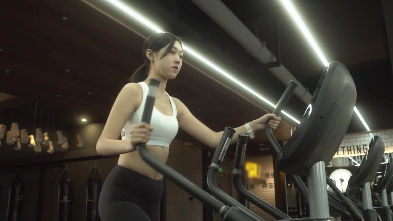 迷人的年轻女性健身在椭圆机健身在健身房视频素材