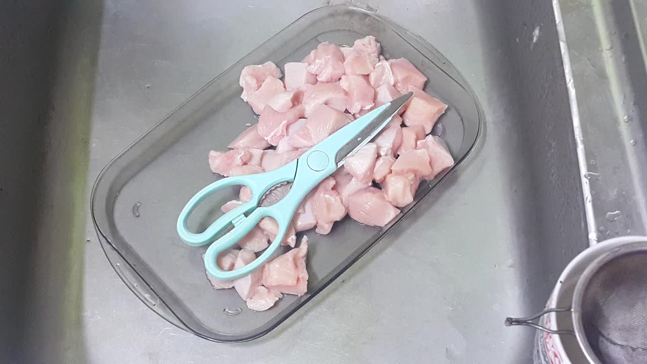 在厨房里用锋利的食物剪刀把鸡肉切成小块。视频下载