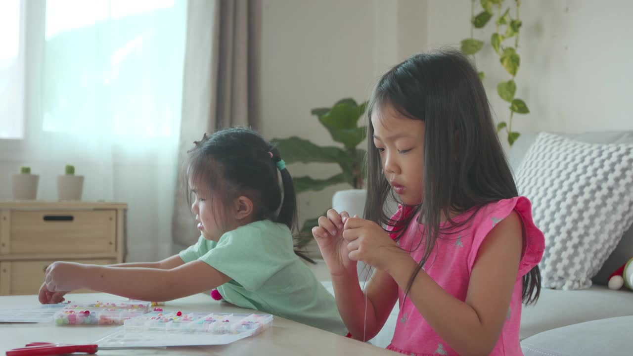 亚洲女孩和朋友把珠子串在一起，在家里有意图和乐趣。孩子创造手工手镯，以发展手的能动性视频下载