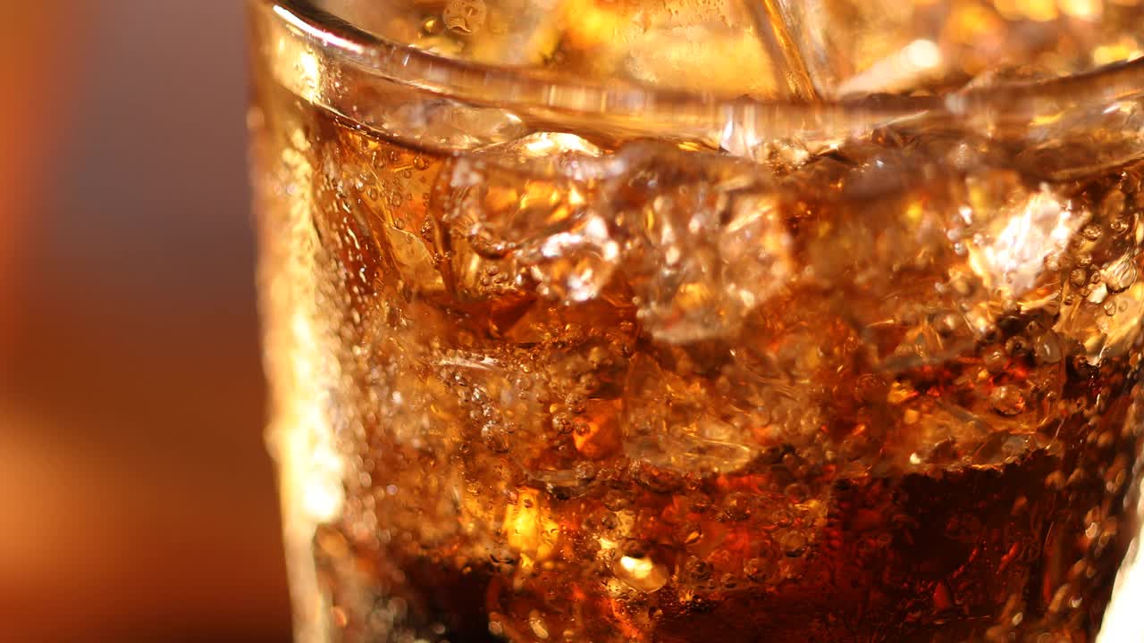 一杯有冰块的可乐。可乐饮料与冰和泡沫在玻璃近距离。在模糊的背景上旋转可乐杯。慢动作旋转4K视频片段视频下载