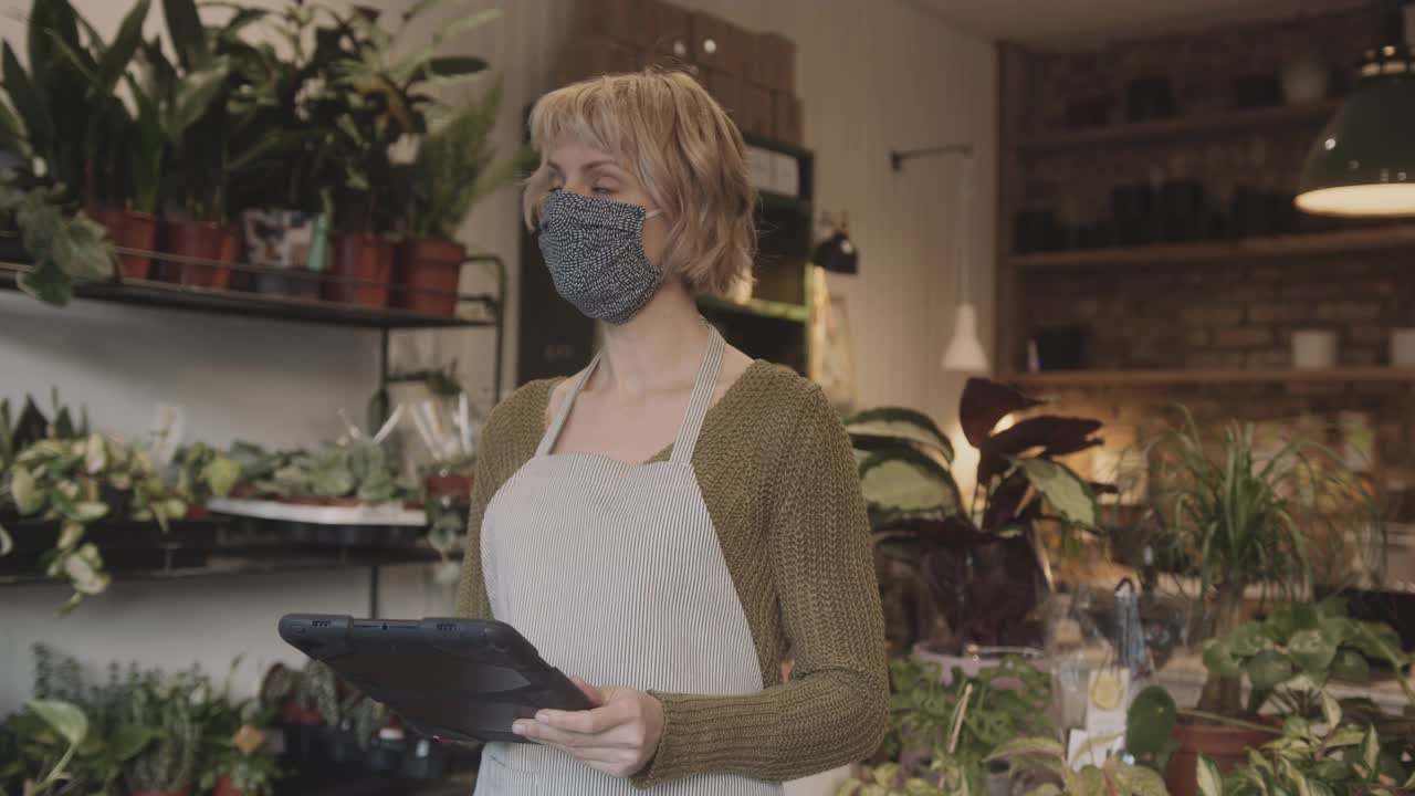 成年女性小企业主戴着防护口罩和围裙在商店里用平板电脑清点存货视频素材