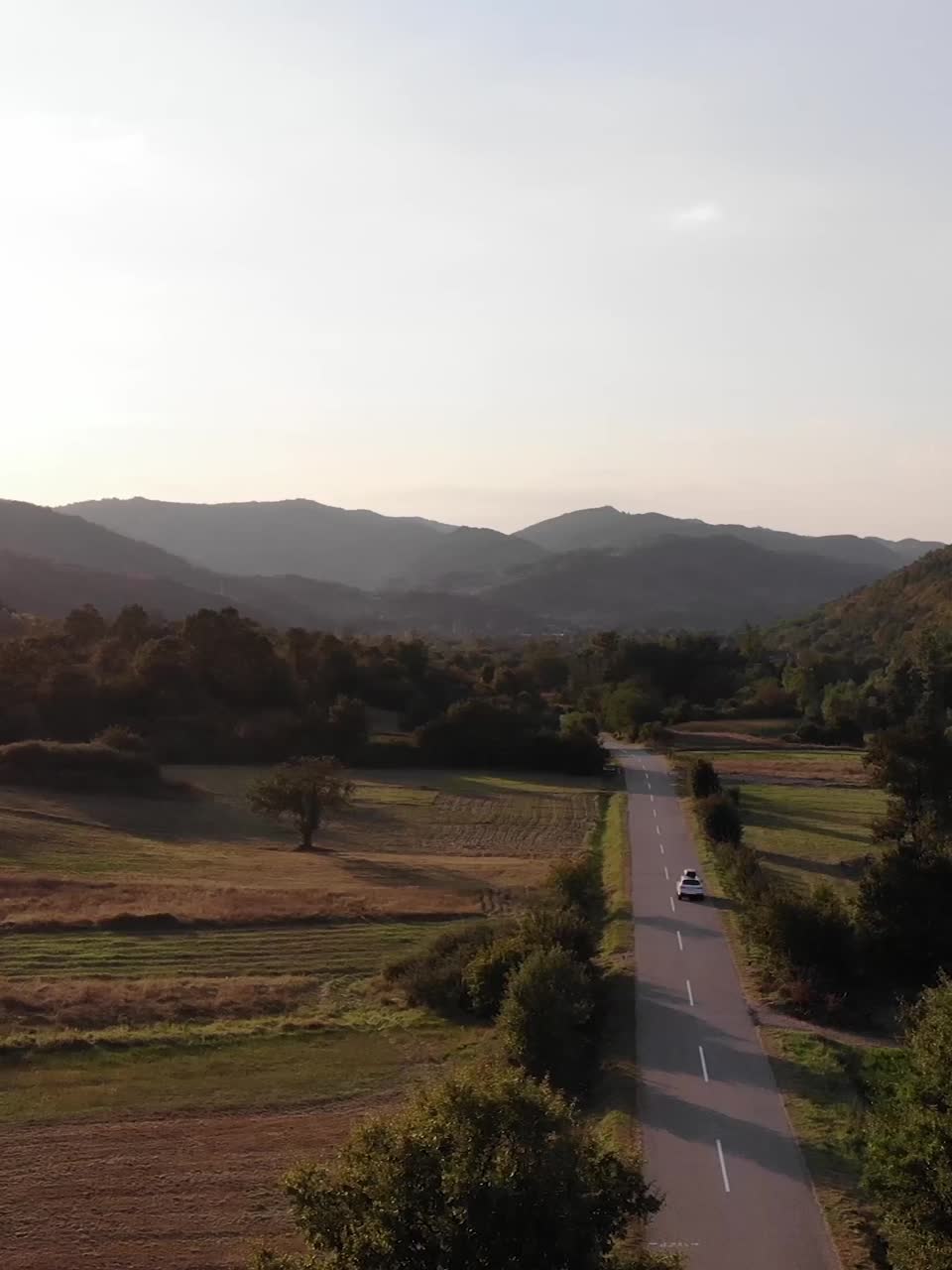 由无人机拍摄的垂直4k视频。汽车驶入金色的夕阳中。俯视图美丽的自然和救济-东欧-塞尔维亚视频素材