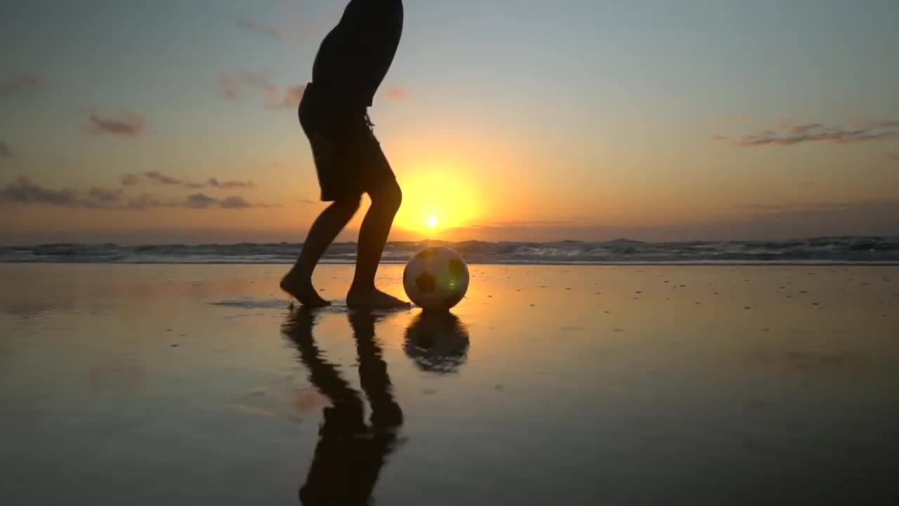 日出时，男孩在沙滩上踢足球视频素材