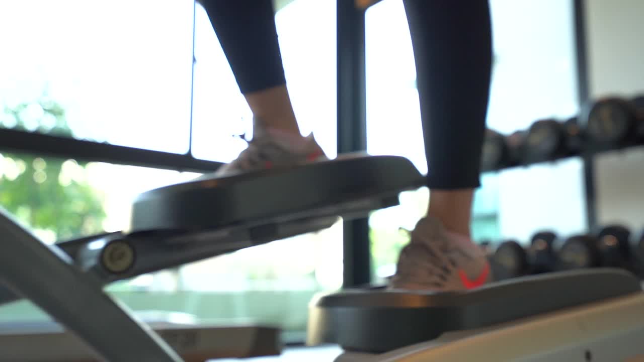 在健身房跑步机上跑步或走路的运动鞋接近女性的腿。视频素材