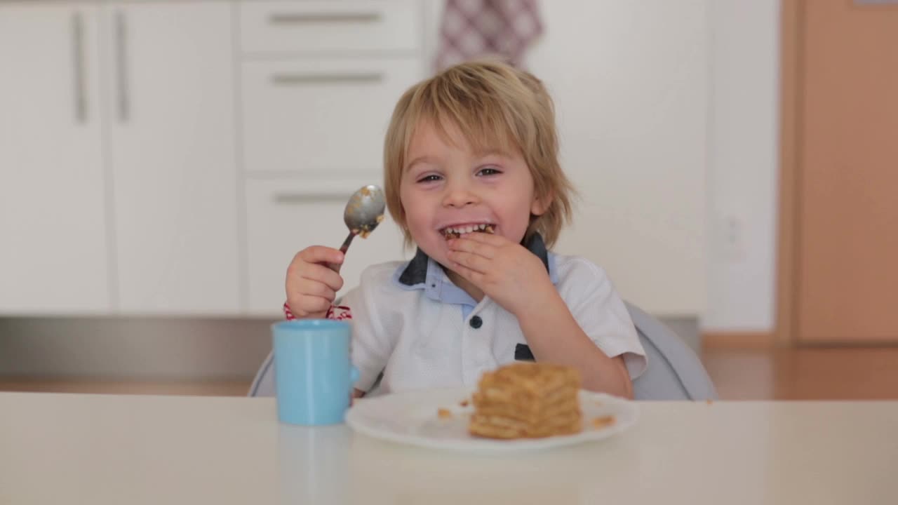 可爱的学前班男孩，金发碧眼的孩子，在家里吃着蛋糕喝着牛奶，开心地笑着视频素材