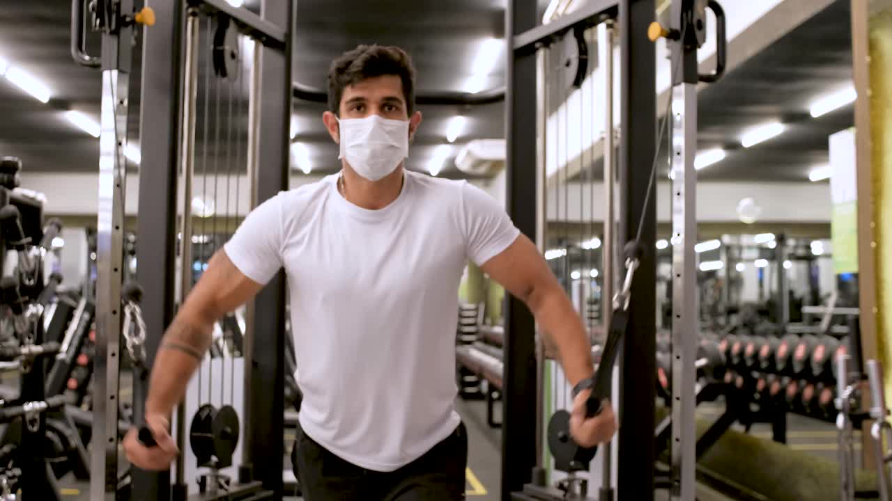 戴着防护面罩的男子在健身器材中锻炼肩膀和胸部肌肉视频素材
