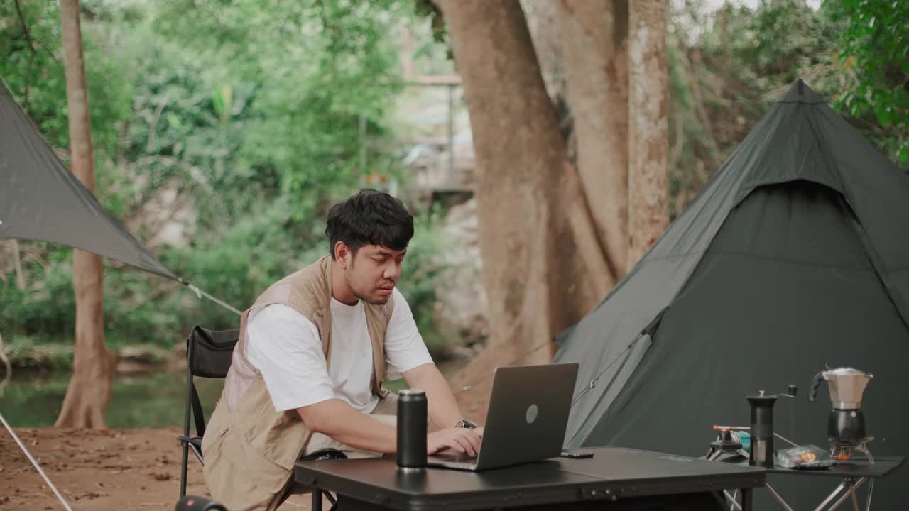 一个用笔记本电脑工作的人在露营时观察大自然视频下载