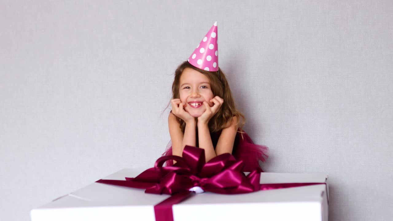 快乐的小女孩的肖像在粉红色的裙子和帽子把她的胳膊肘放在大礼物盒视频下载