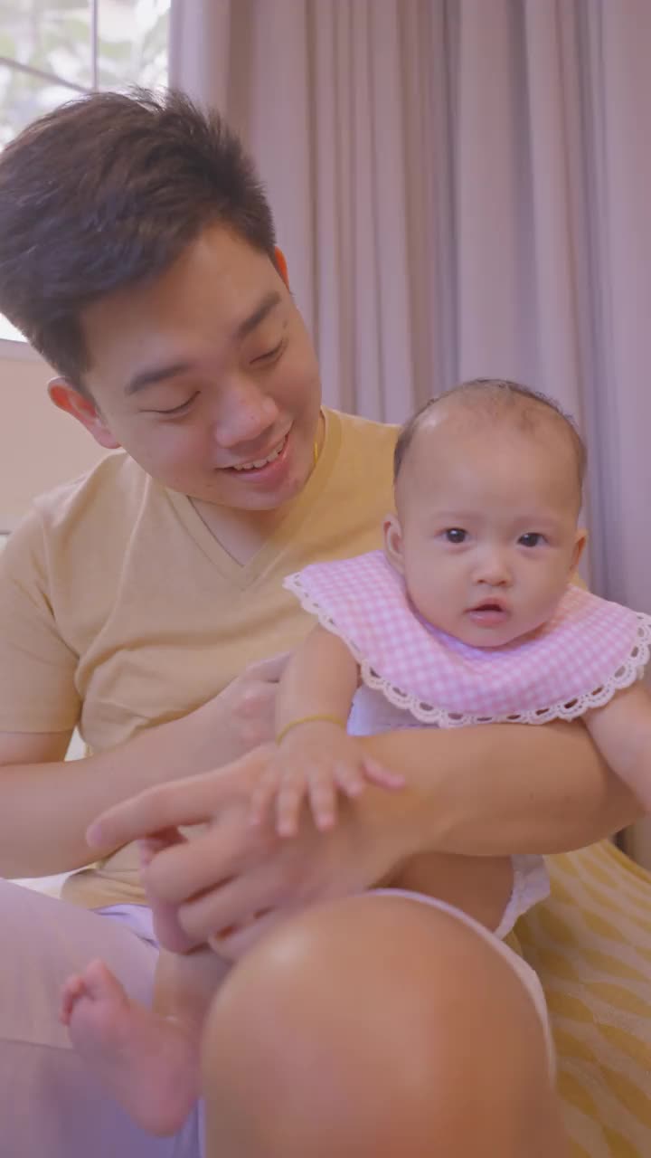 亚洲家庭有一个女婴，父亲和女儿宝宝在他的膝盖上玩，在客厅感受积极的情绪，幸福的时刻。视频购买