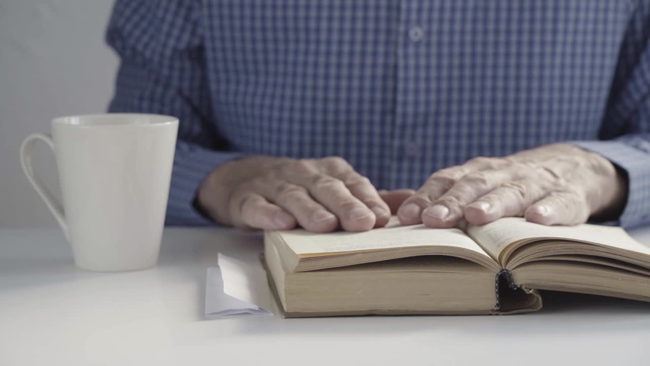 一位老人的手放在一本打开的书上。概念:老年人读物。教育的概念。人类手中的旧书视频素材