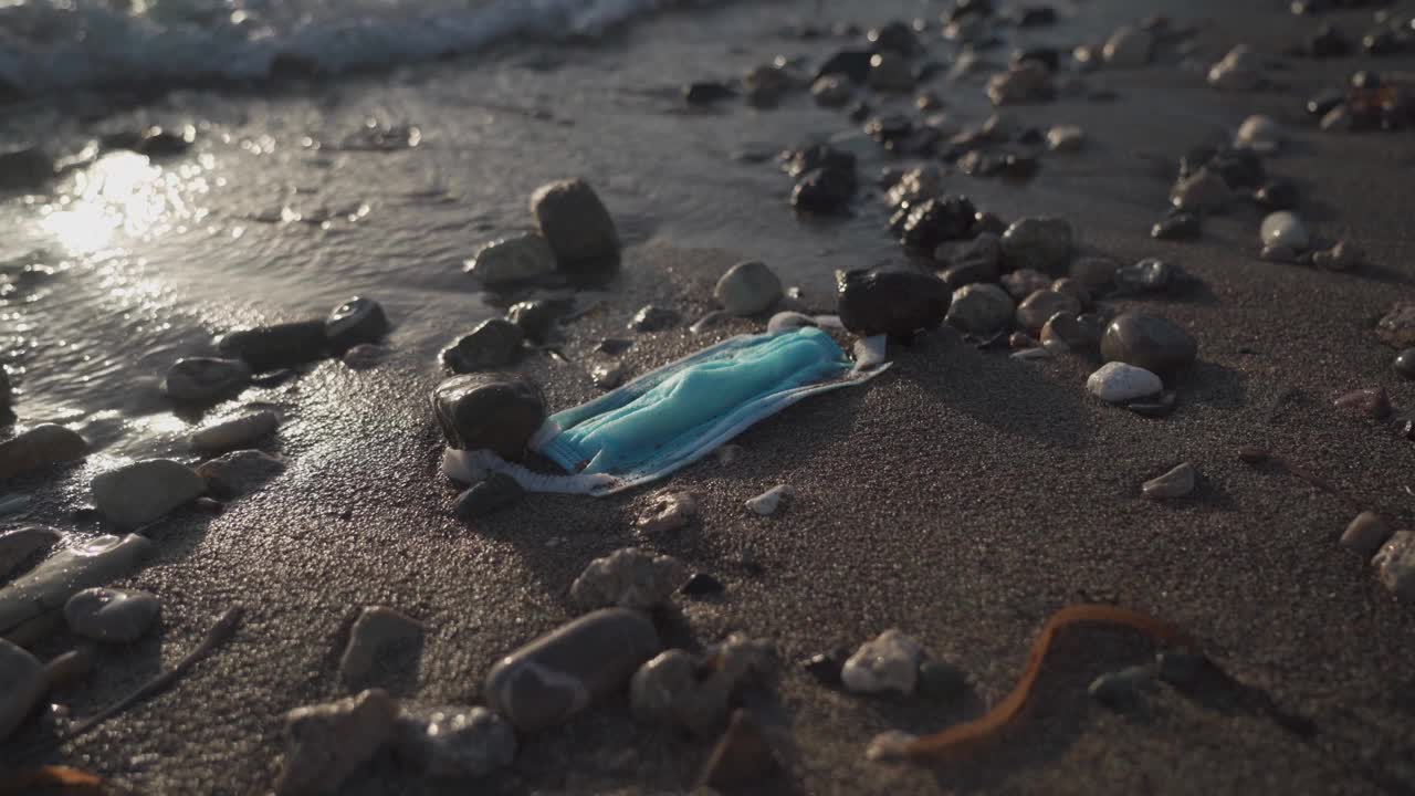 蓝色医用口罩从海上抛向海滩。医疗用品的物品和废物处理。停止水和海洋污染。新冠肺炎后的污染。浪费在冠状病毒。海洋污染视频素材