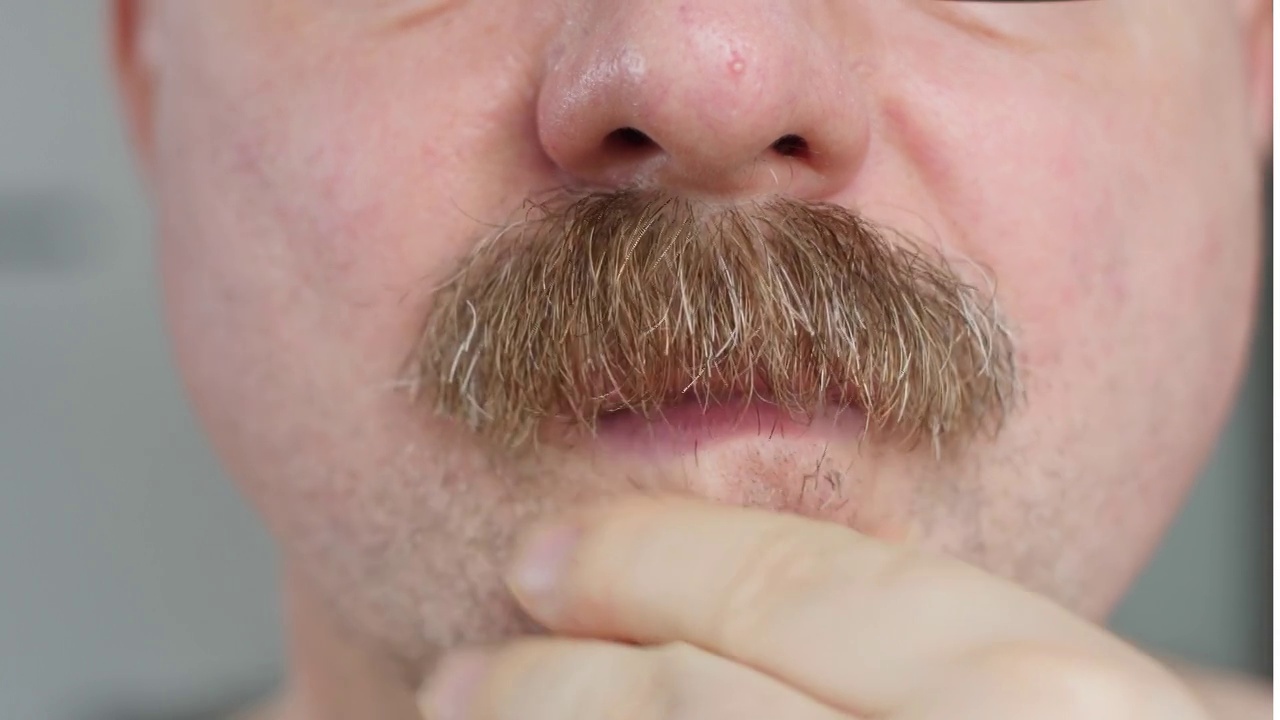 一个男人用电动剃须刀刮他的胡子。面部毛发微调。近距离视频下载