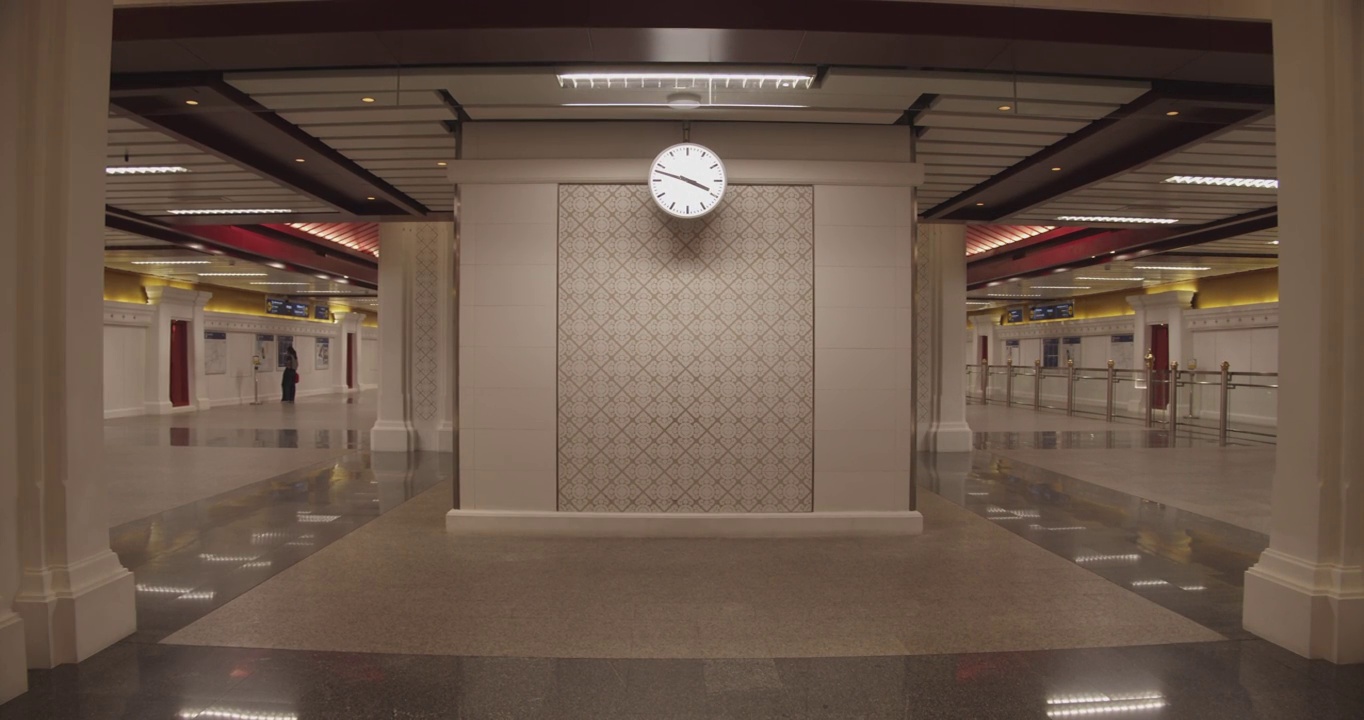 在一个灯光明亮、中心有时钟的火车站里，一个男人在框架里行走视频下载